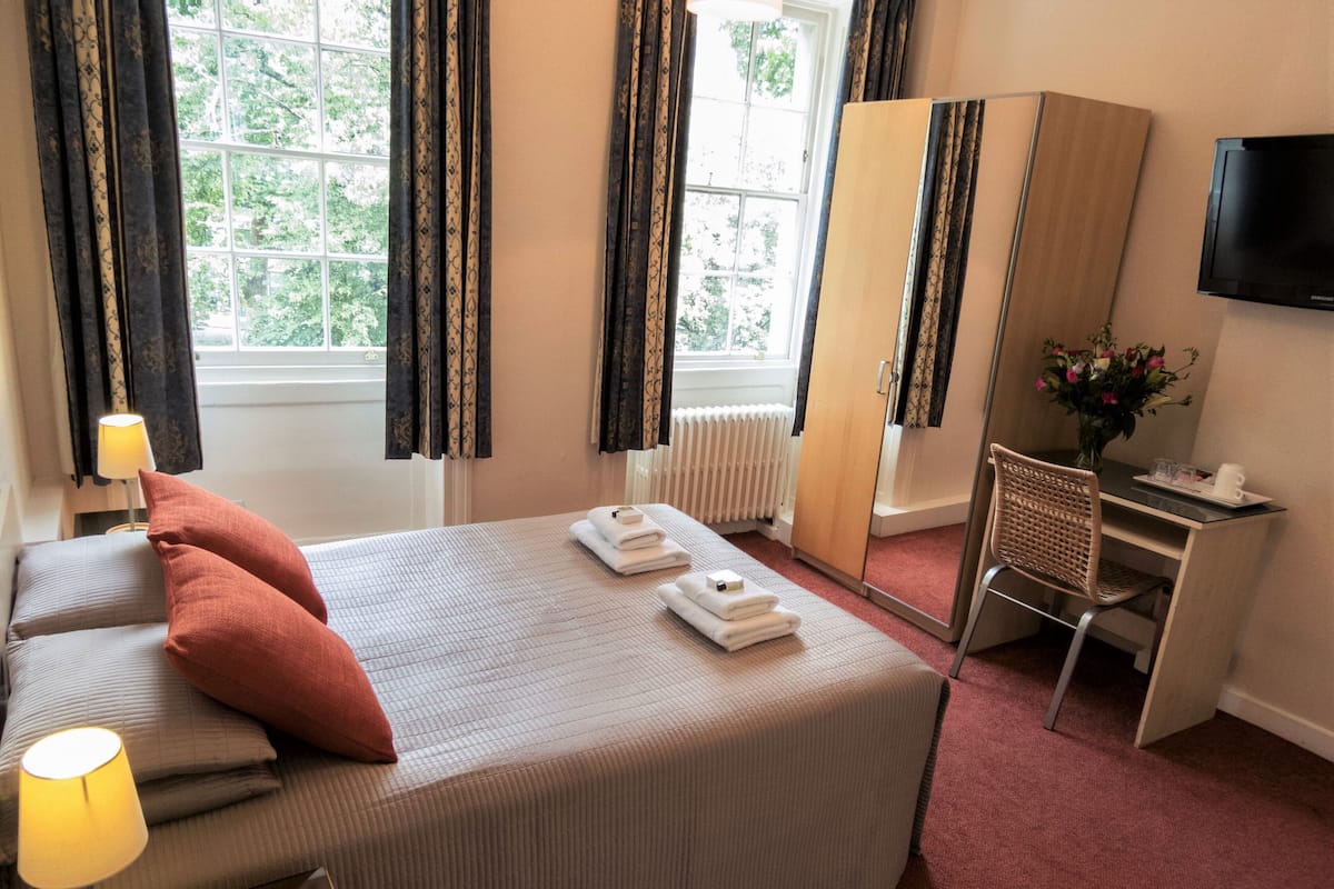 Ein Hotelzimmer mit Bett, Schreibtisch, Stuhl, Fernseher und einem Fenster mit Vorhängen.
