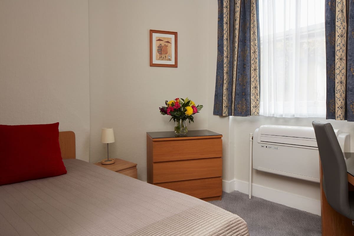 Ein Hotelzimmer mit Bett, Nachttisch, Kommode, Schreibtisch und Heizkörper.