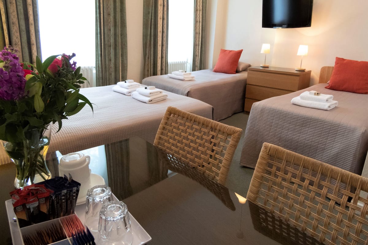 Ein Hotelzimmer mit zwei Betten, einem Fernseher, einem Tisch mit Blumen und einem Fenster mit Vorhängen.