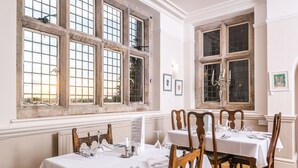 A dining area with tables set for a meal, large windows with multiple panes, and framed artwork on the walls. - The Amberley Inn (Stroud)