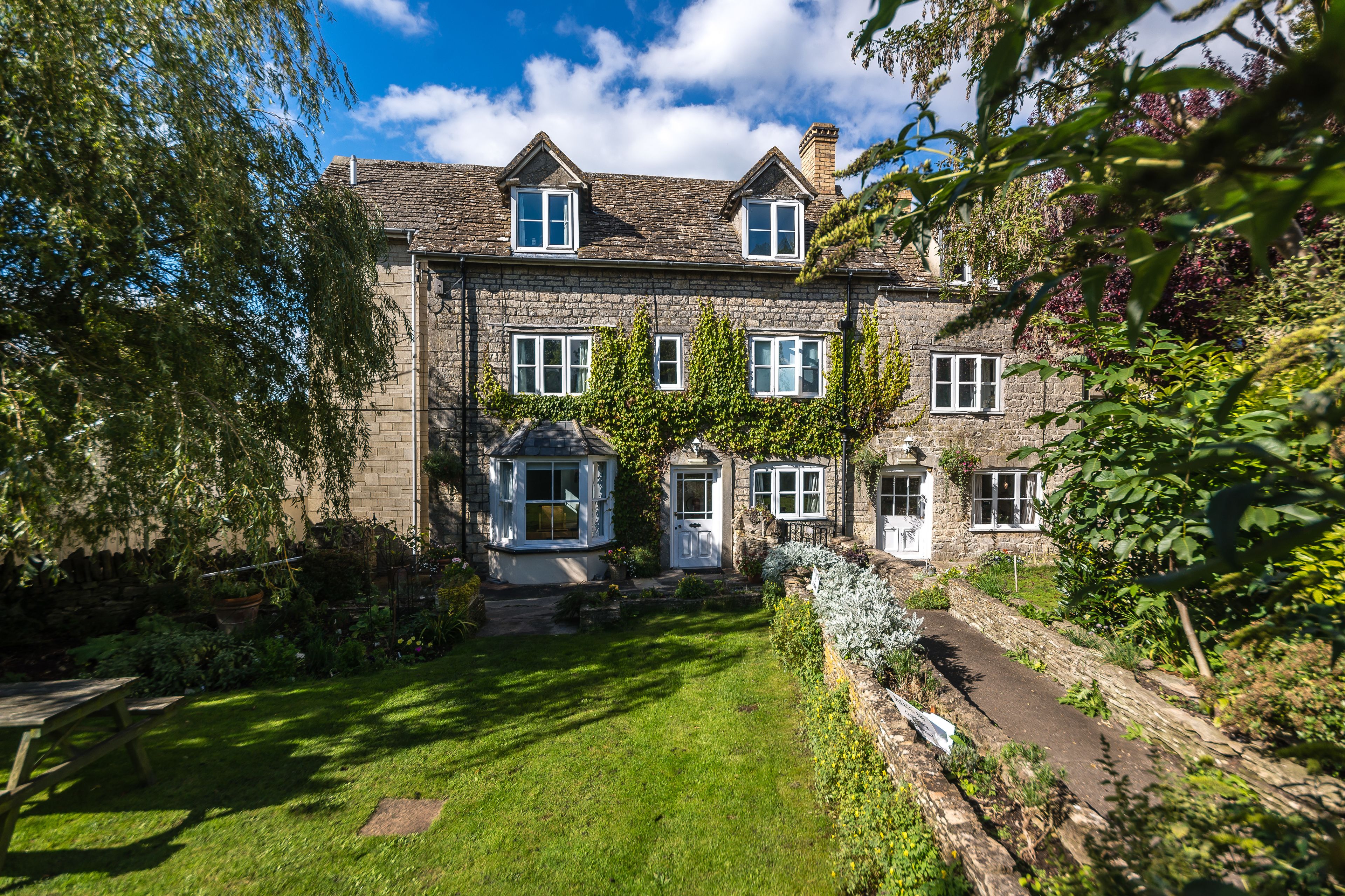 A stone house with a garden, a paved driveway, and a picnic table.