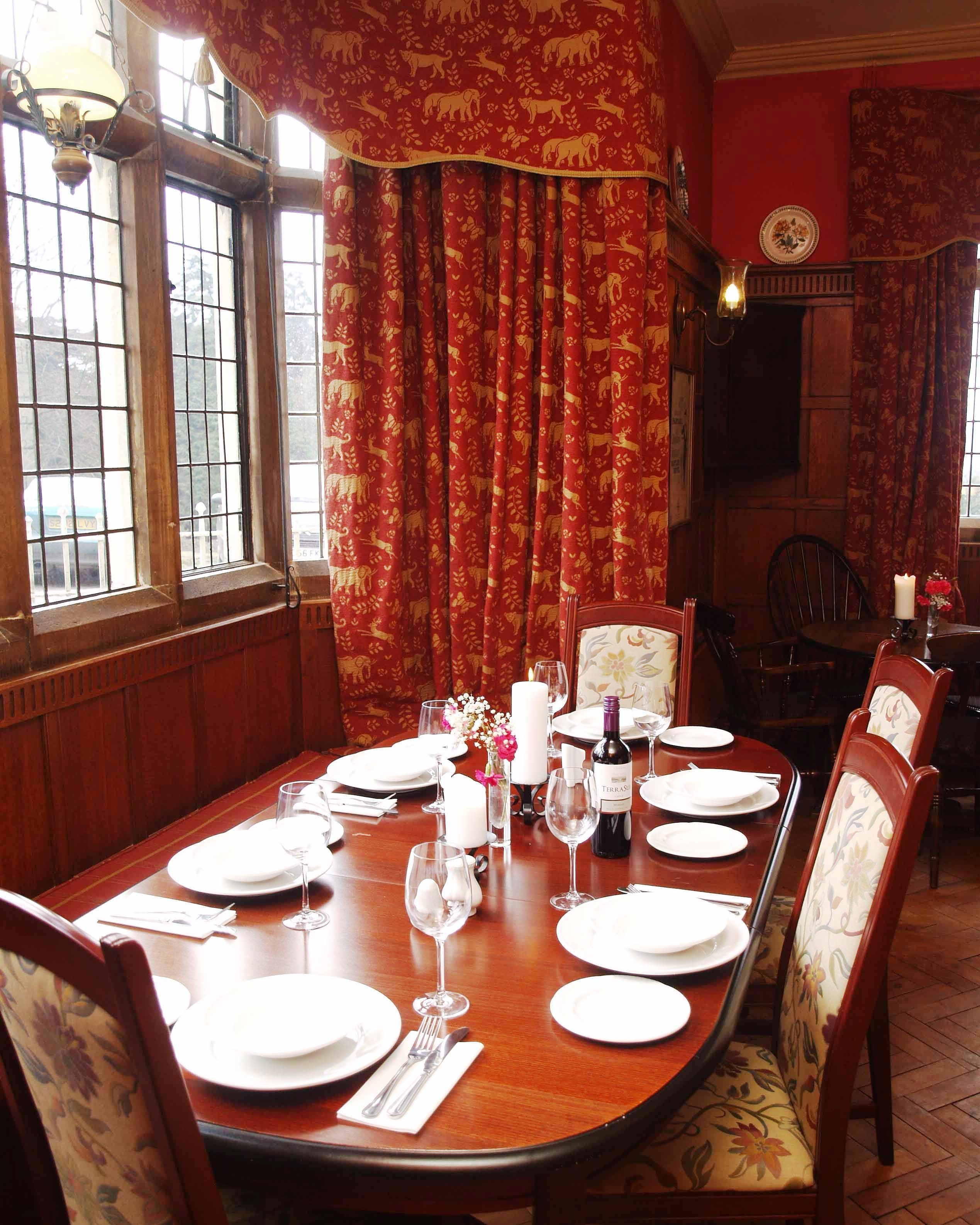 Comedor con mesa de madera dispuesta para una comida, cortinas rojas y un candelabro.