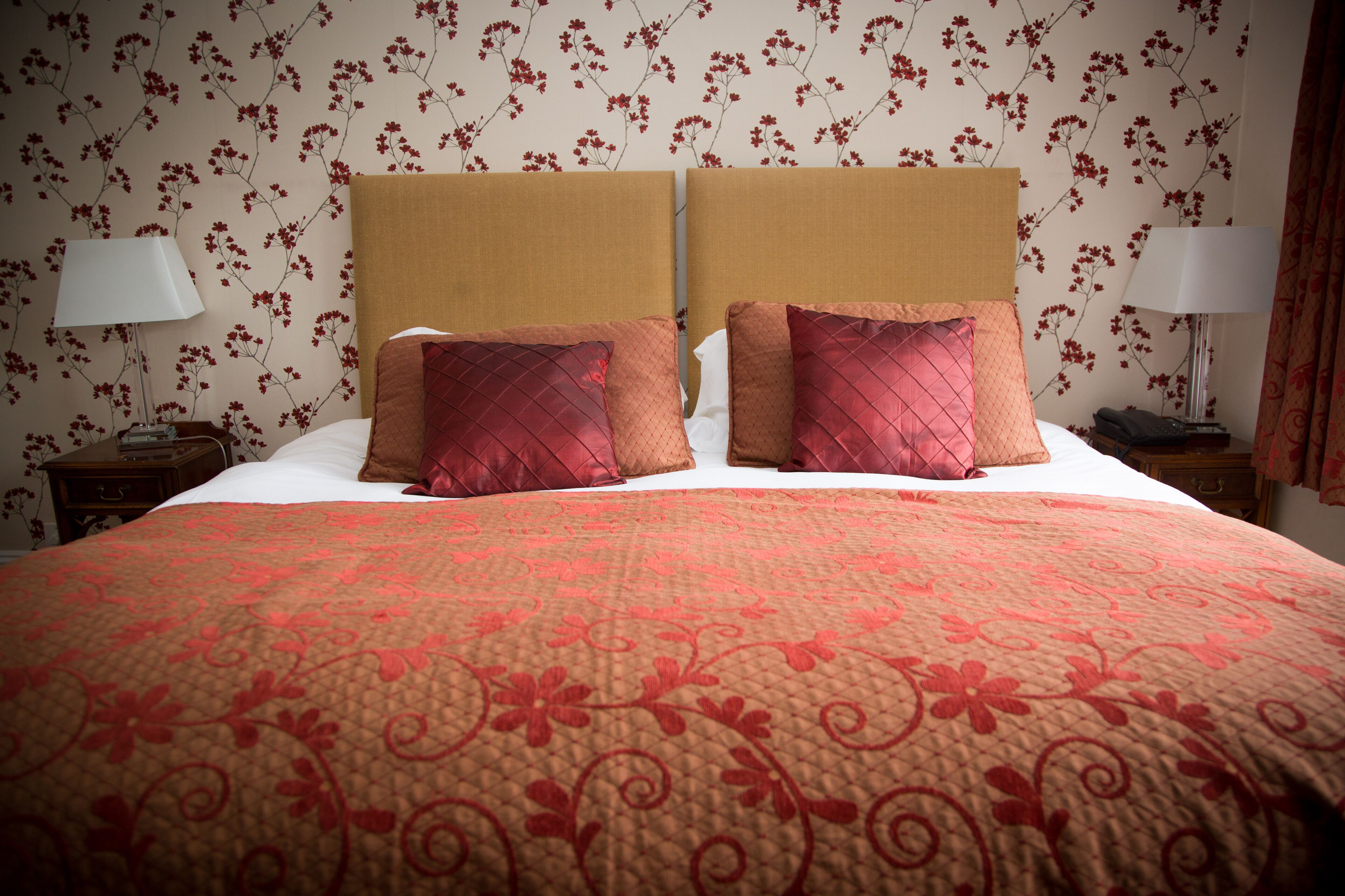 A double bed with a floral-patterned headboard, two nightstands with lamps, and a floral wallpaper.