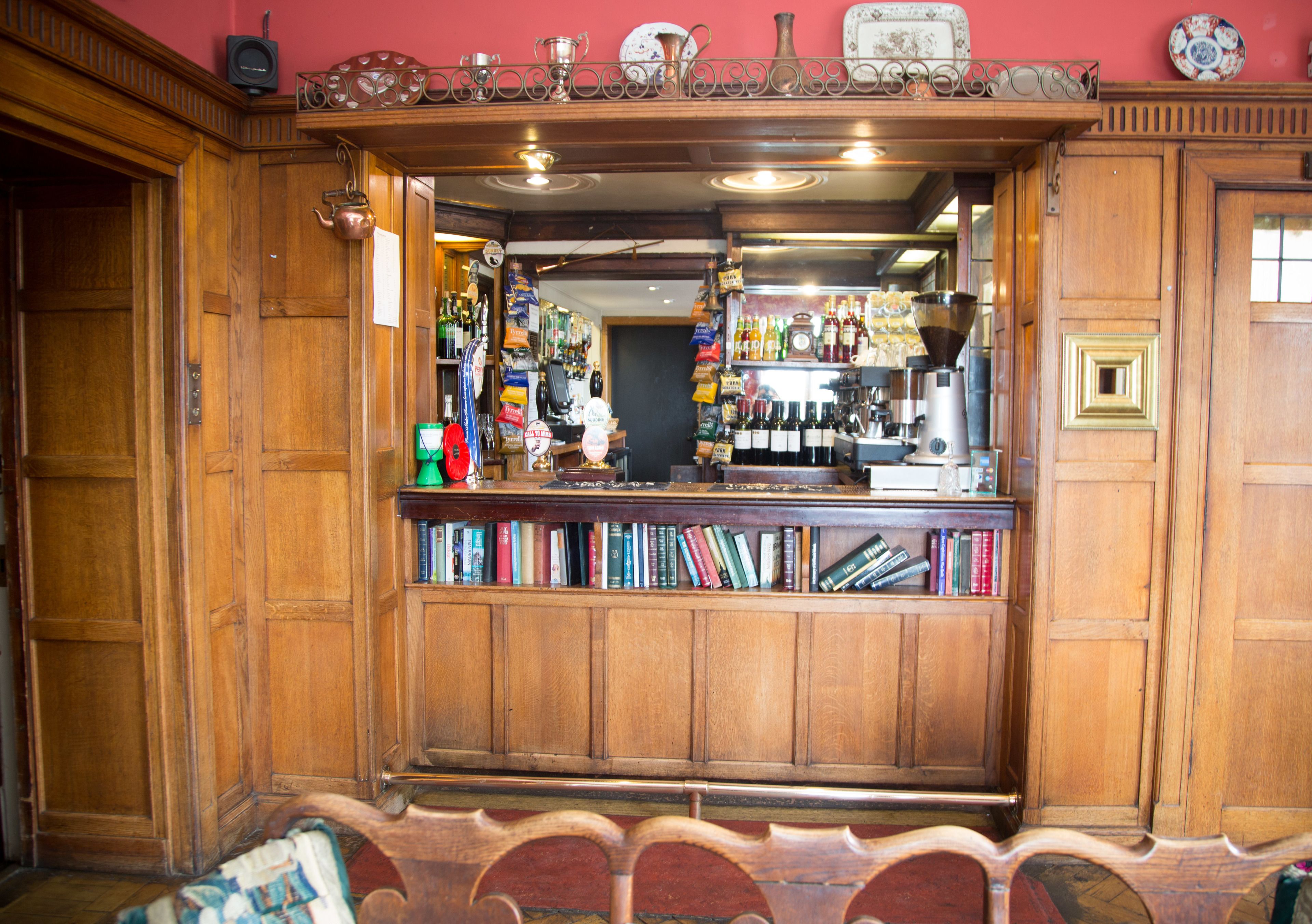 Una zona de bar con paneles de madera, estanterías llenas de libros y varias botellas.