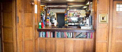 Un espace bar avec des lambris en bois, des étagères remplies de livres et diverses bouteilles.