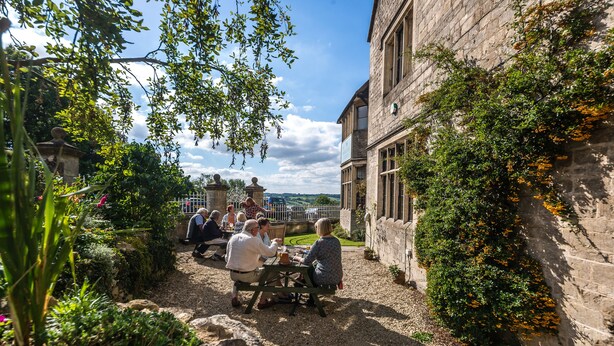 A courtyard with a stone building, a gravel path, and a group of people sitting at a table. - The Amberley Inn (Stroud)