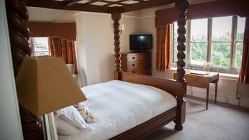 A four-poster bed with a television in the corner, a desk, and a window with curtains.