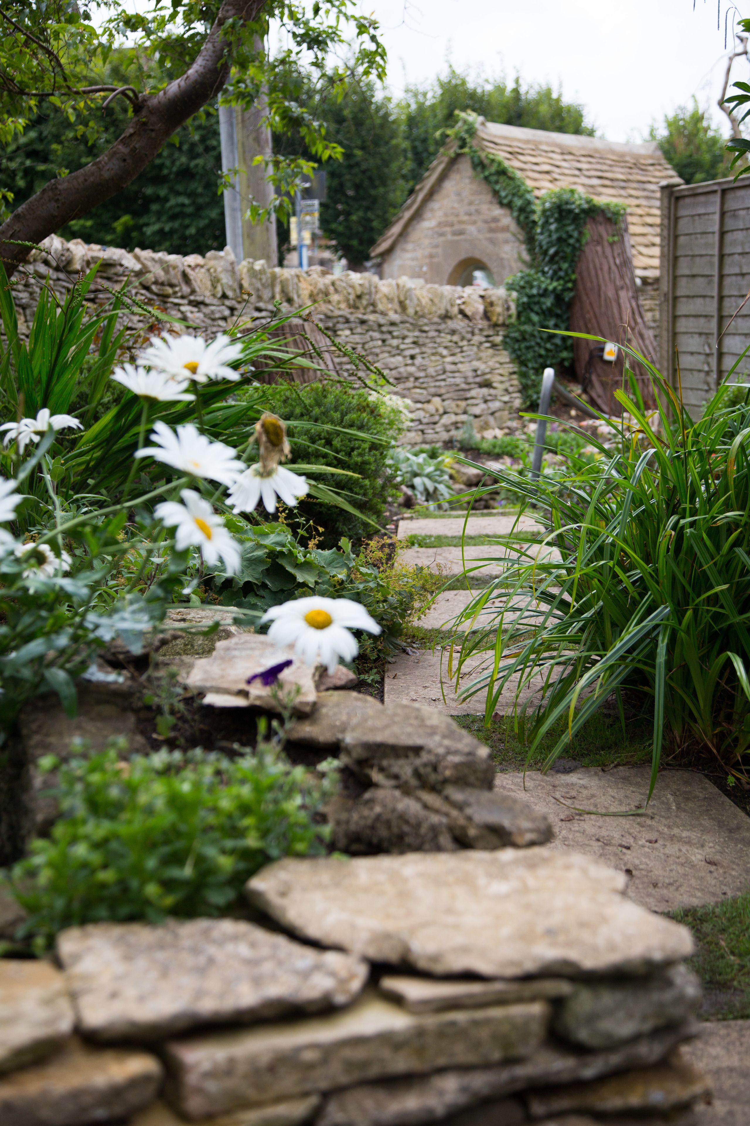 Ein Garten mit weißen Blumen, einer Steinmauer und einem rustikalen Gebäude im Hintergrund.