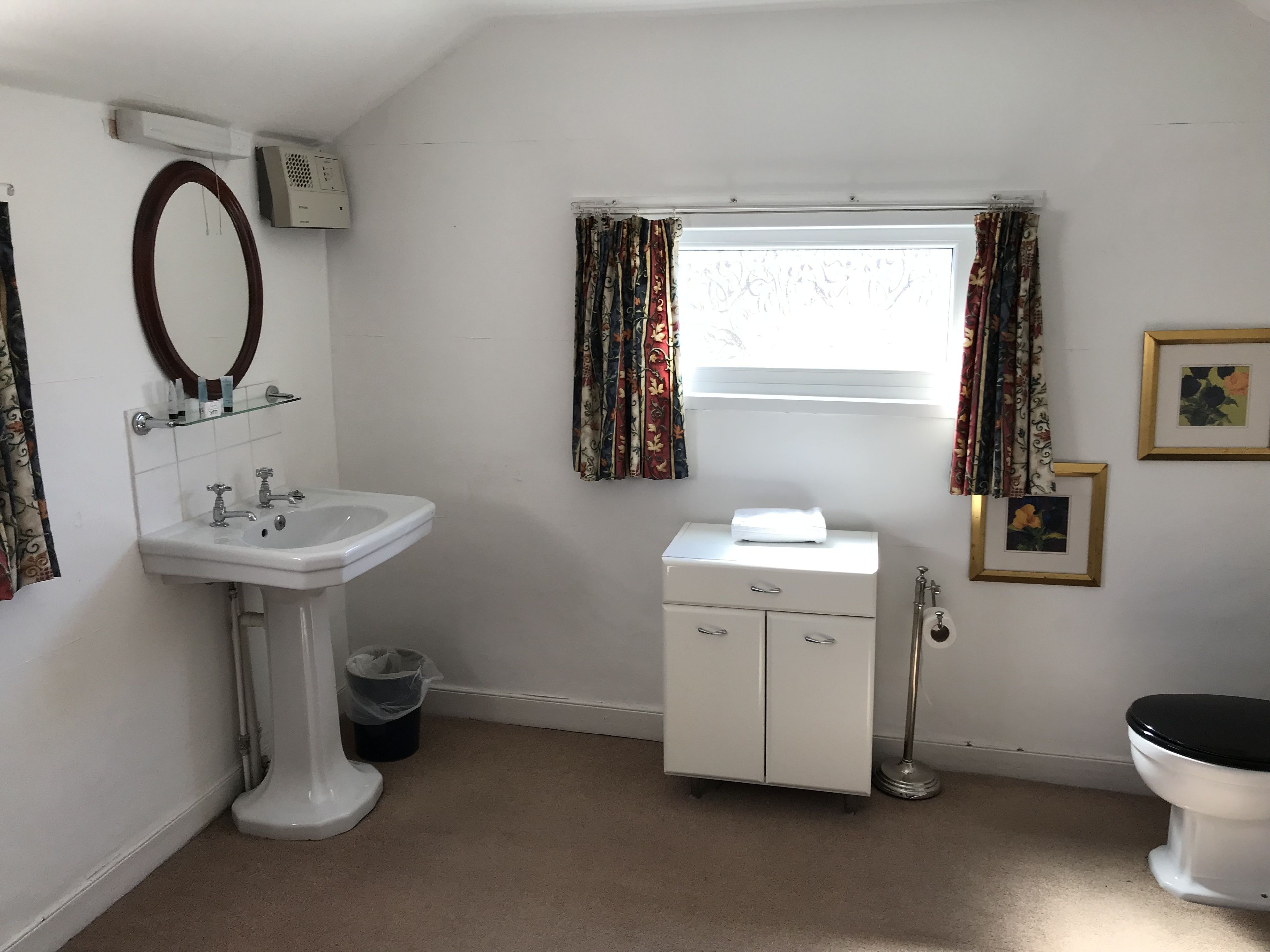 A bathroom with a white sink, toilet, and cabinet, a mirror, and patterned curtains.