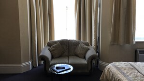 A corner room with a sofa, a small round table, and a bed. - The Embassy Hotel (Great Yarmouth)