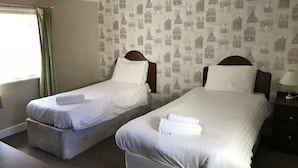 A double room with two single beds, a window with green curtains, a lamp on the nightstand, and a wall with Paris-themed wallpaper. - The Embassy Hotel (Great Yarmouth)