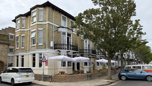 A corner building with a cafe on the ground floor, a car parked on the street, and a tree in front. - The Embassy Hotel (Great Yarmouth)