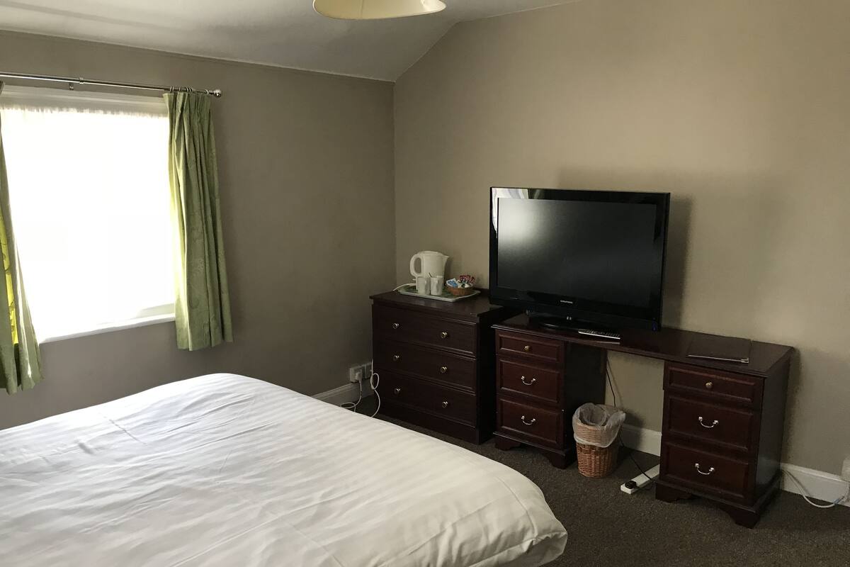 A hotel room with a bed, a television, a dresser, and a window with curtains.