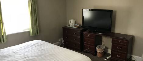 Una habitación de hotel con una cama, televisión, cómoda y ventana con cortinas.