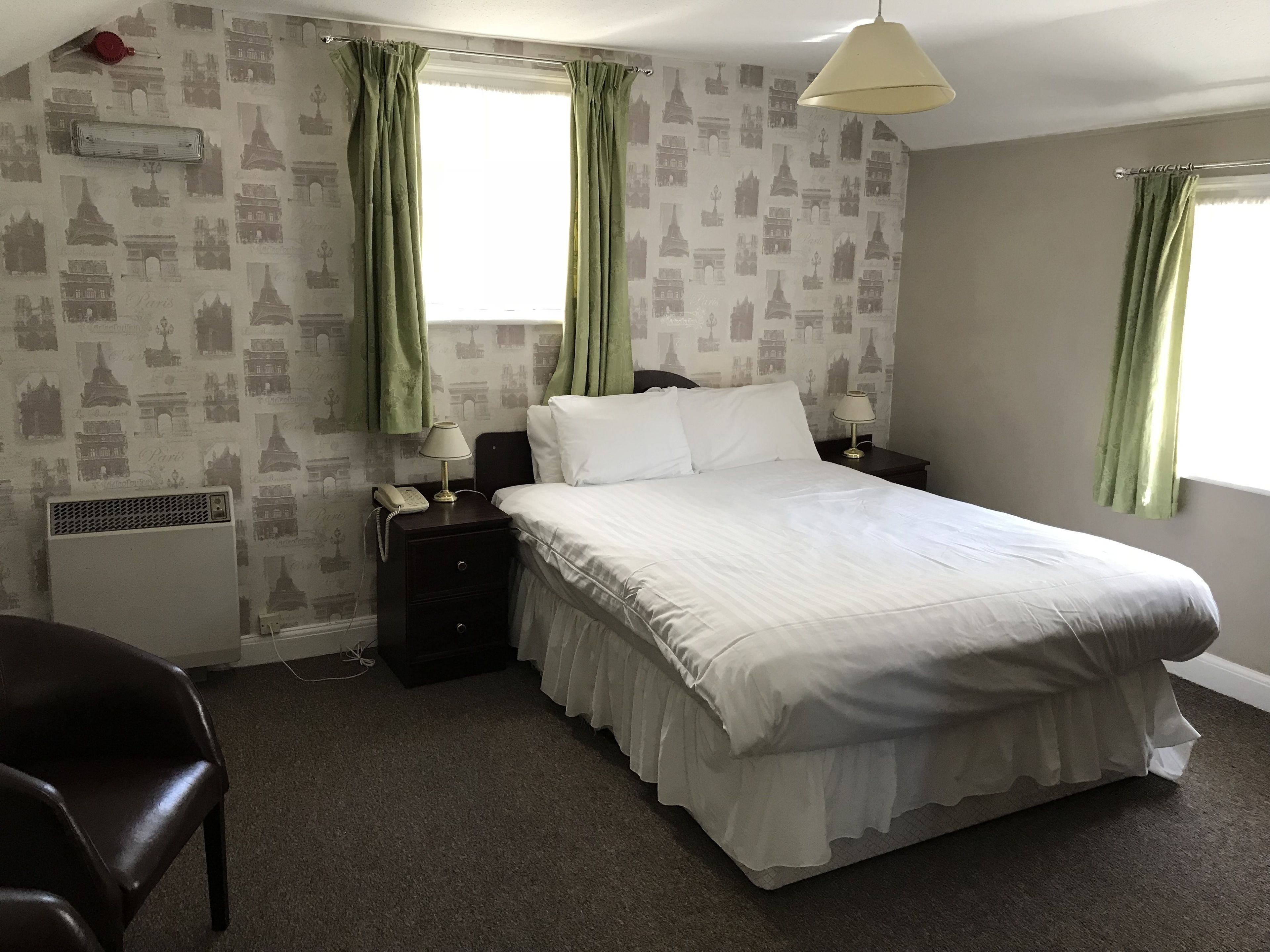 A neatly arranged hotel room with a large bed, two bedside tables with lamps, a chair, and a radiator.