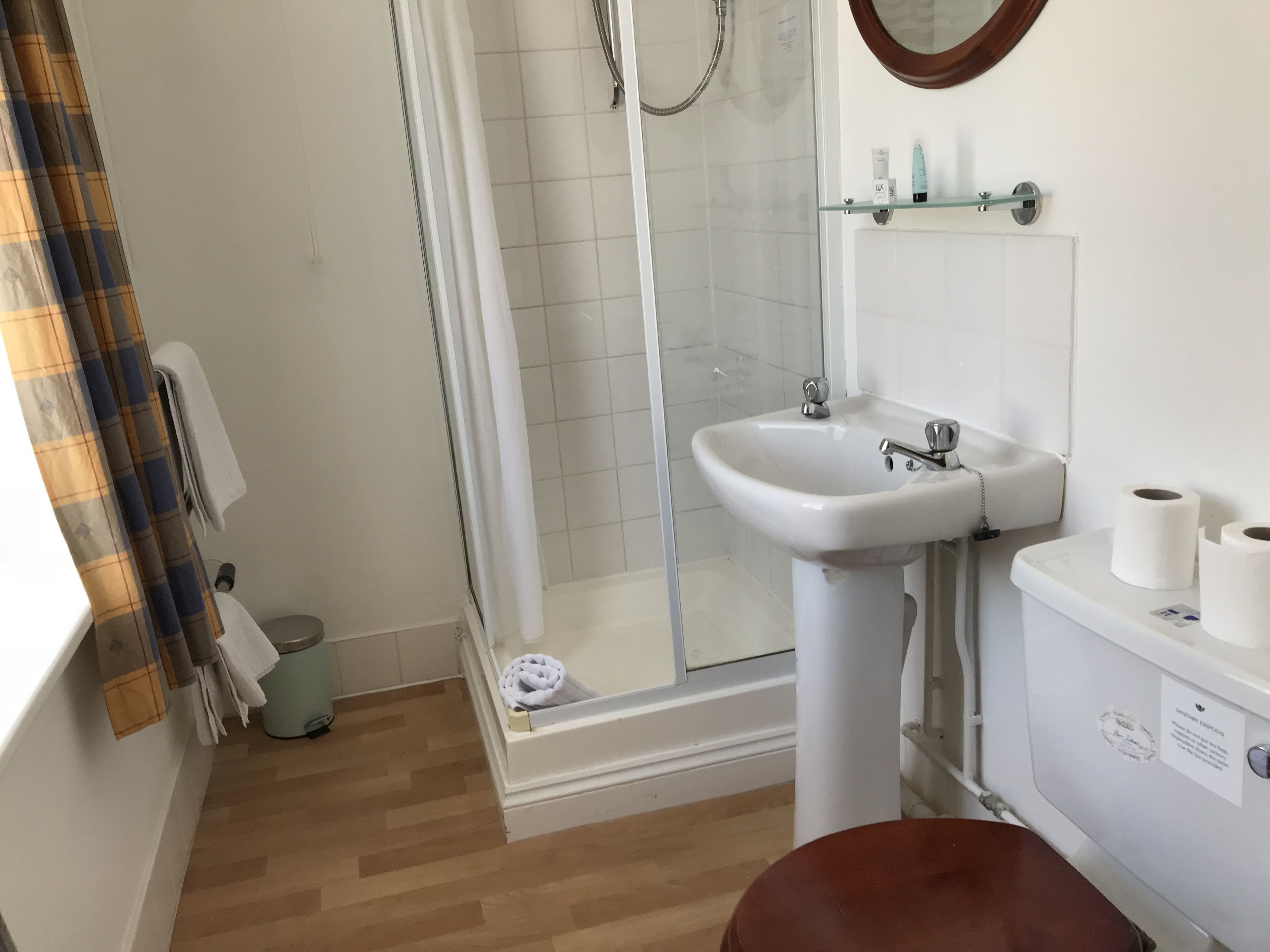 A bathroom with a shower, sink, toilet, and a wooden floor.