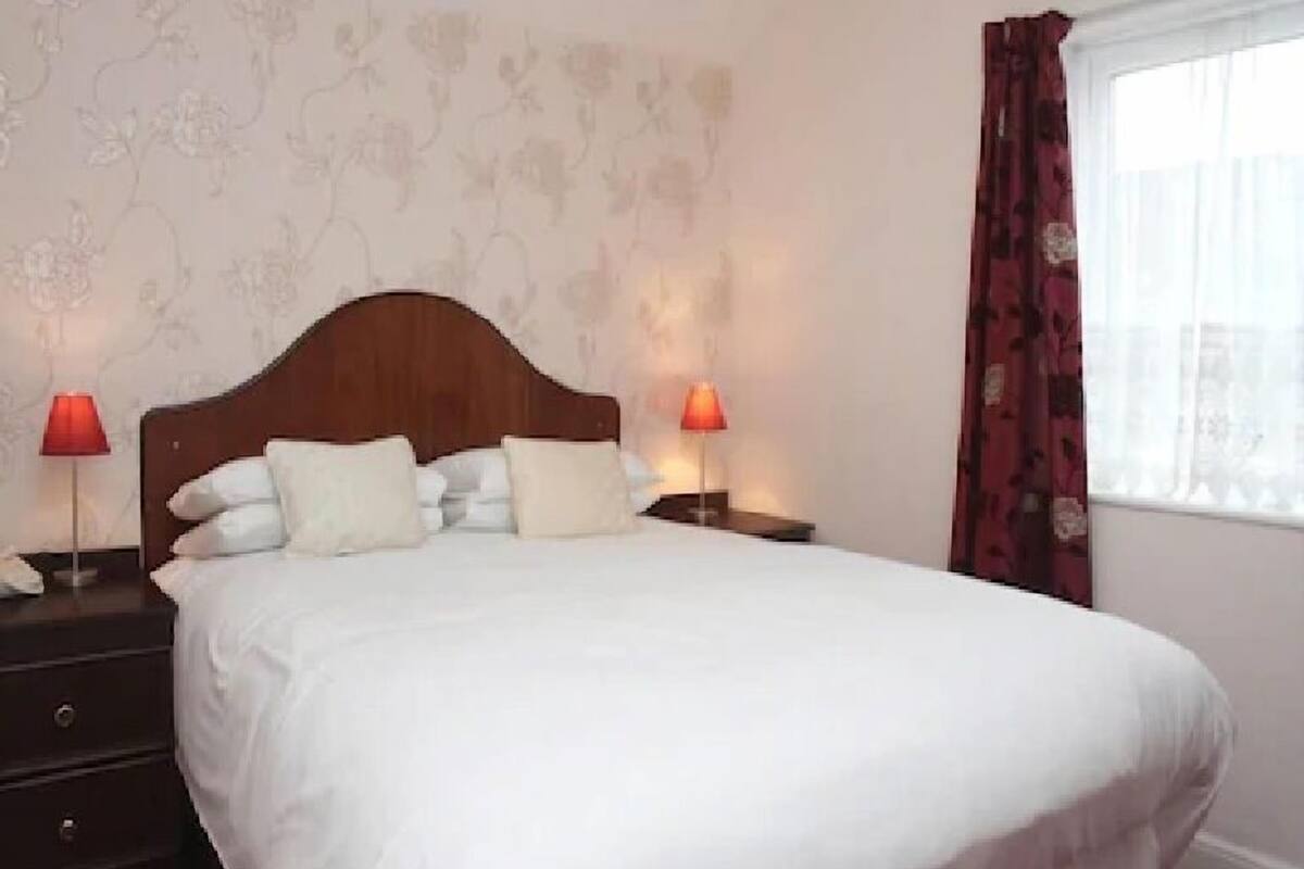 A neatly made bed with white linens, two bedside tables with lamps, and a floral wallpaper pattern on the wall.