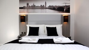 Ein Hotelzimmer mit einem großen Bett, zwei schwarzen Kissen, weißer Bettwäsche und Blick auf eine Stadtlandschaft mit Brücke und Kirchturm.