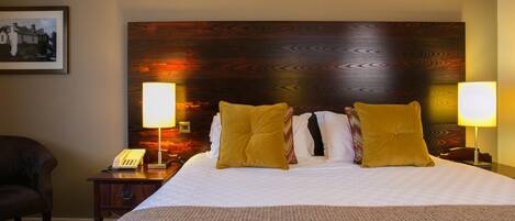 A hotel room with a large bed, two bedside lamps, a telephone, and a framed picture on the wall.