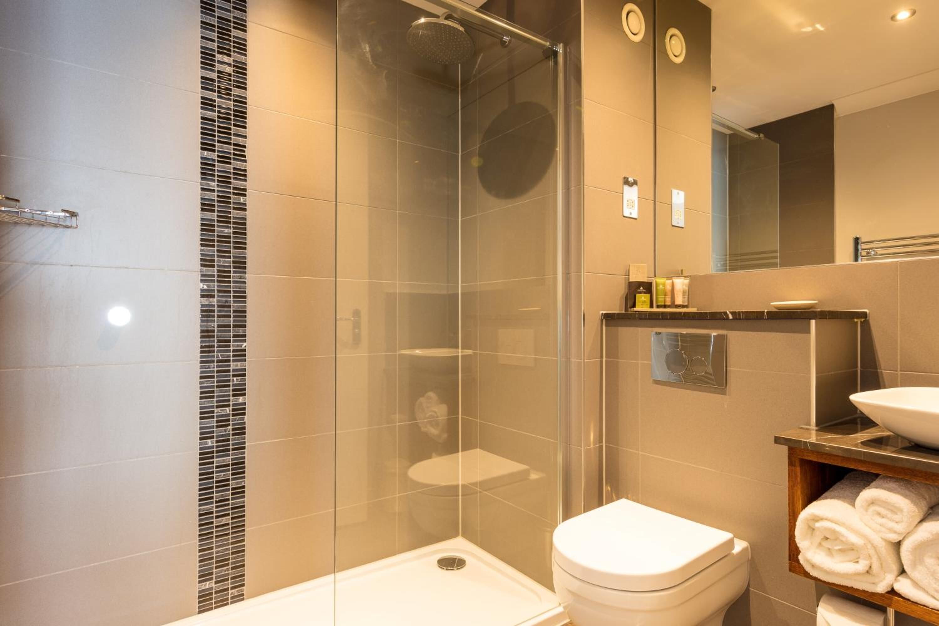 A modern bathroom with a glass-enclosed shower, a toilet, and a sink with a mirror above.