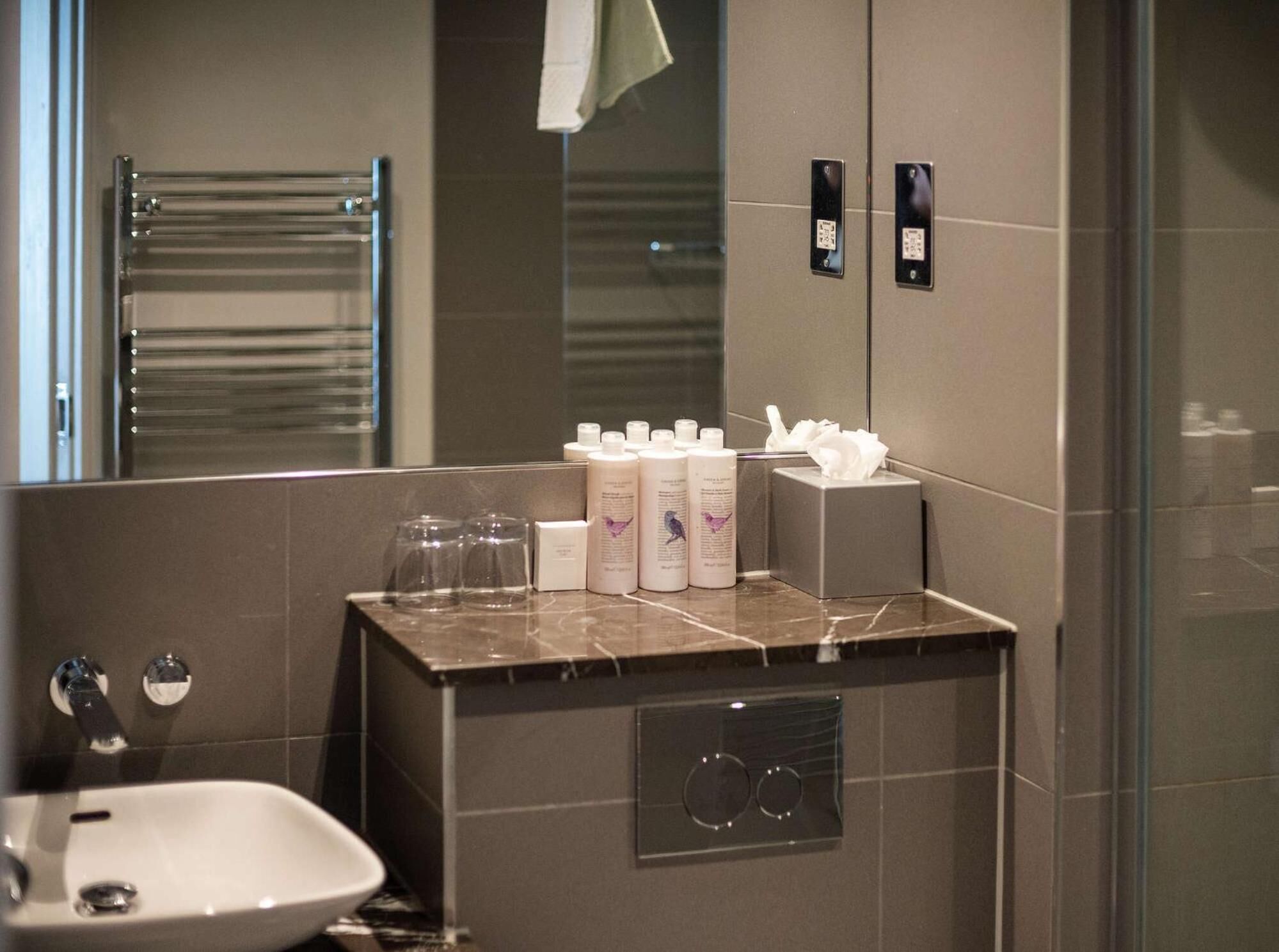 Een moderne badkamer met een marmeren wastafel, een wasbak en een spiegel. Er staan toiletartikelen op de wastafel, een handdoekhouder en een douchecabine met glazen wanden.