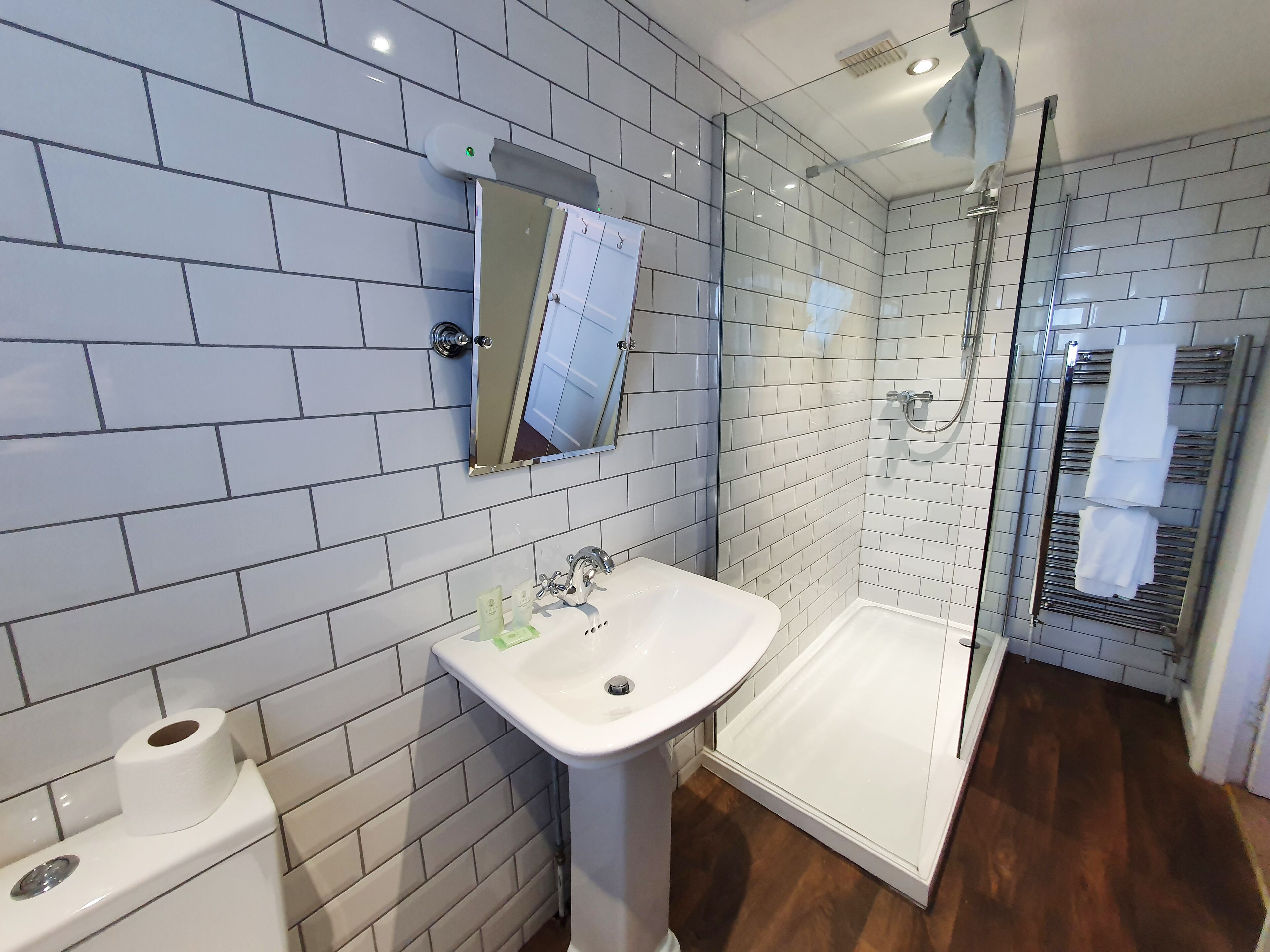 Une salle de bain moderne avec des murs recouverts de carreaux blancs, un lavabo sur pied, une cabine de douche en verre et un porte-serviettes.