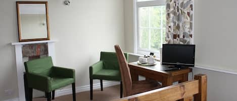 Una habitación con dos sillas verdes, una mesa de madera con un televisor, un espejo y una ventana con cortinas.