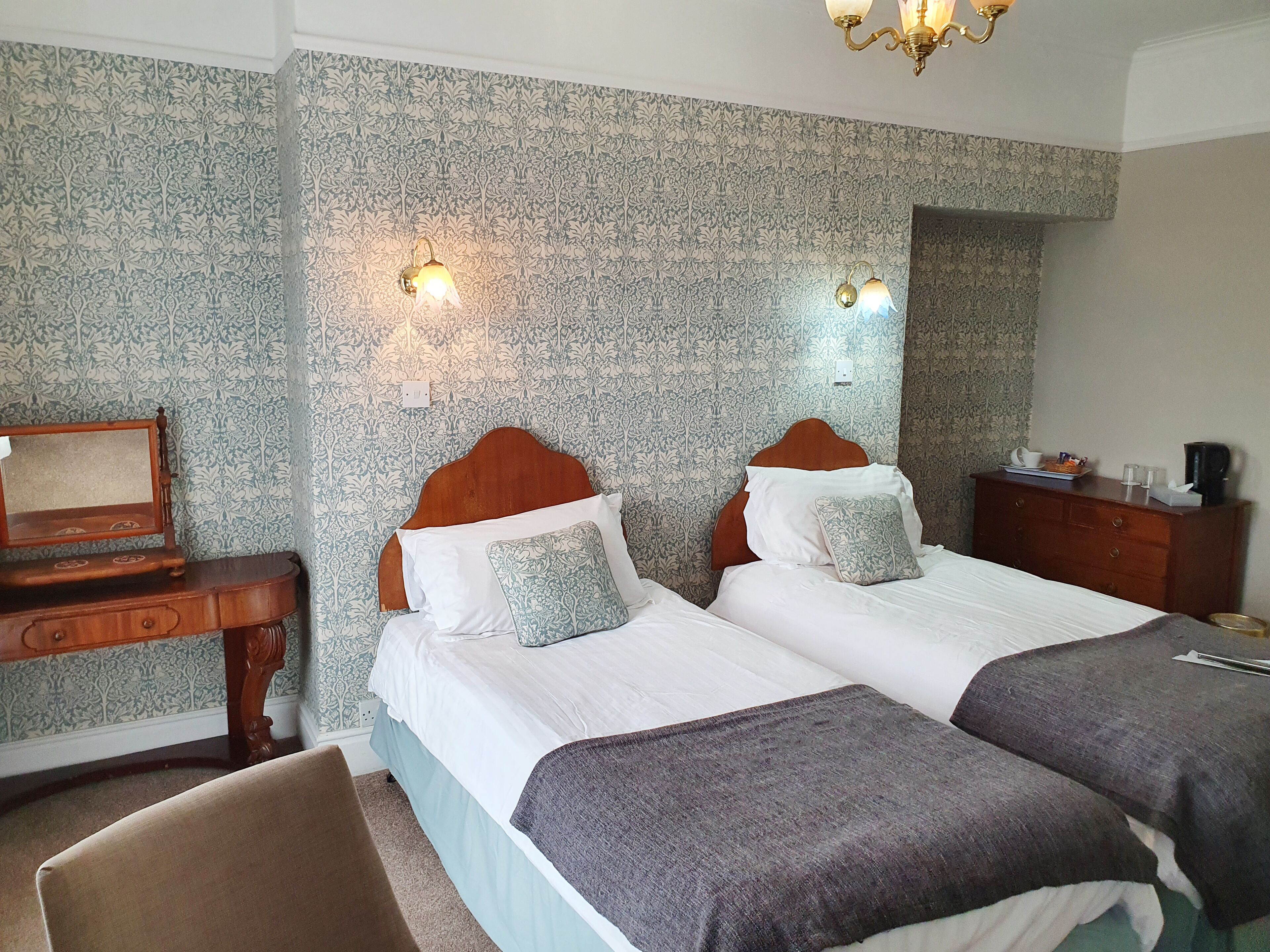 A hotel room with two beds, a wooden dresser, a desk, and a chandelier.