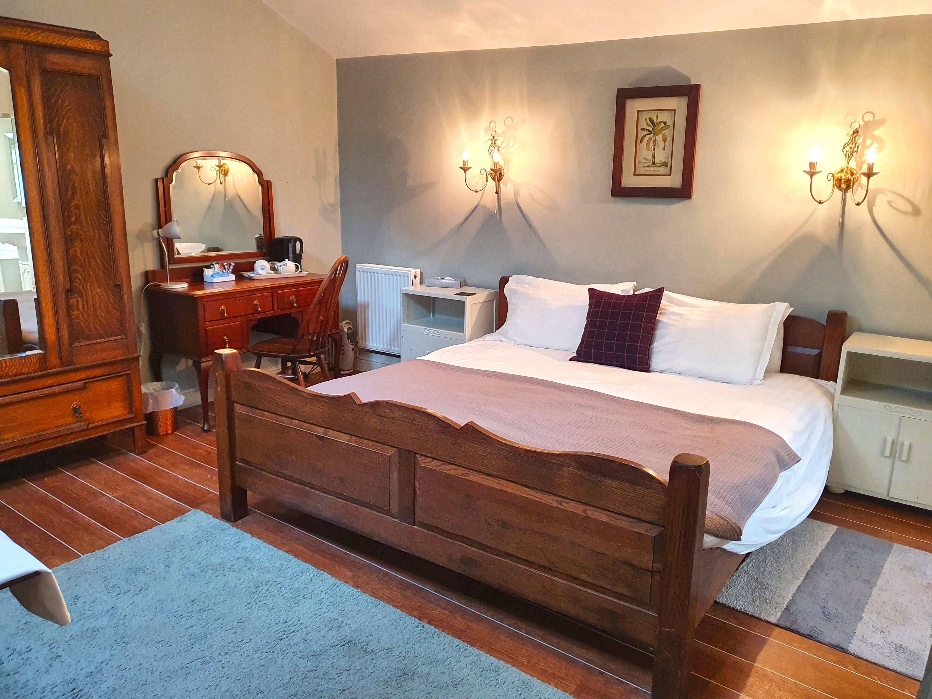 Un dormitorio con cama de madera, cómoda, escritorio, silla, radiador y un cuadro en la pared.