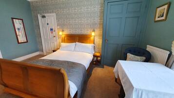 Een slaapkamer met een houten bed, een klein bed, een blauwe deur en een radiator.