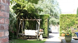 A garden with a brick wall, a wooden arbor, and a pathway leading to a house.