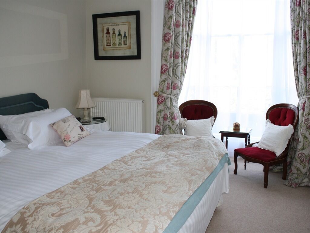 A hotel room with a large bed, a chair, a small table, and curtains.