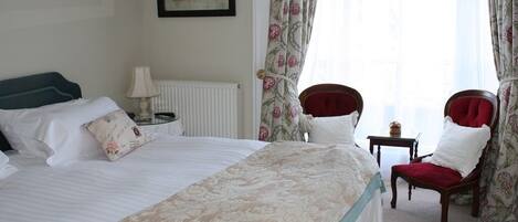 A hotel room with a large bed, a chair, a small table, and curtains.