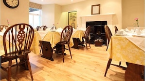 A dining area with wooden chairs and tables, a clock on the wall, and a fireplace.