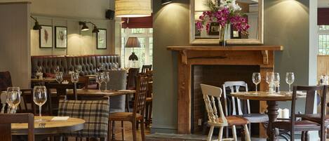 A restaurant interior with wooden furniture, a fireplace, and framed artwork on the walls.