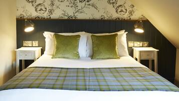 Cama bem arrumada com colcha xadrez, duas almofadas estampadas em verde e duas luminárias de cabeceira em mesas noturnas combinando.