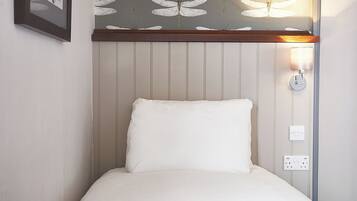 Una cama individual con un almohadón blanco y una manta gris, un aplique de pared y un cuadro enmarcado.