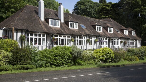 A traditional Tudor-style building with multiple gabled roofs, white-framed windows, and hanging flower baskets. - Dartbridge Inn Buckfastleigh by Greene King Inns (Buckfastleigh)