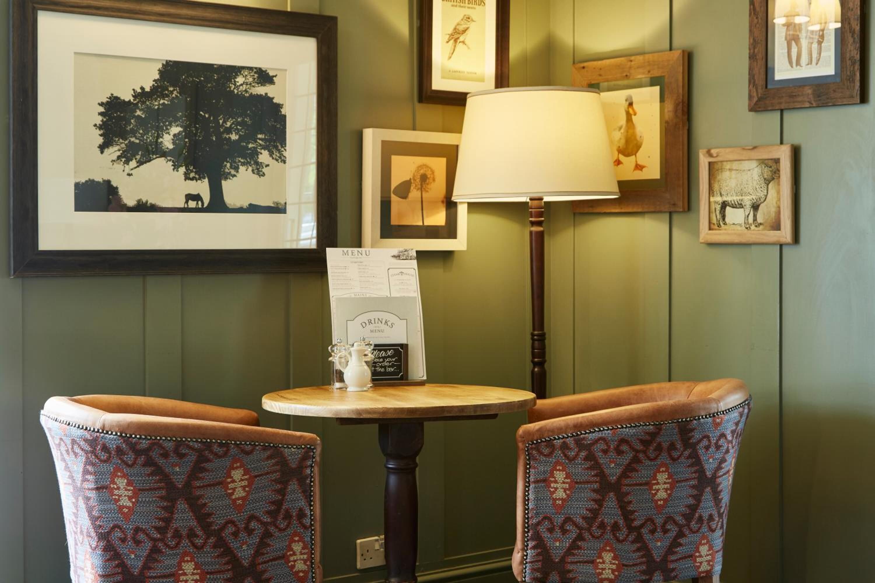 A room with two patterned chairs, a table with a menu sign, and framed pictures on the wall.