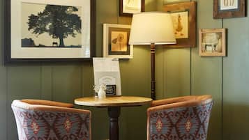 A room with two patterned chairs, a table with a menu sign, and framed pictures on the wall.
