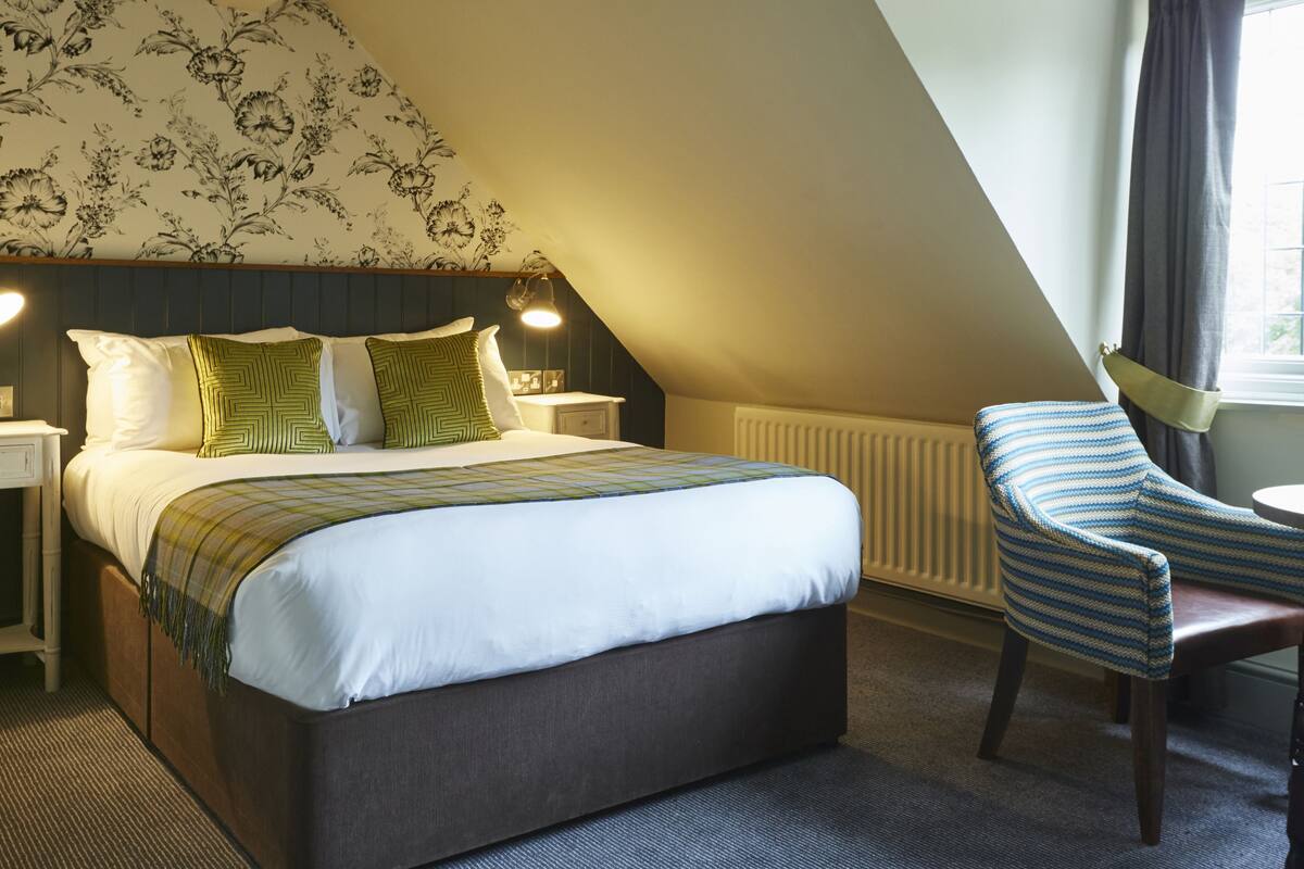 A bedroom with a large bed, a chair, a nightstand, and a window with curtains.