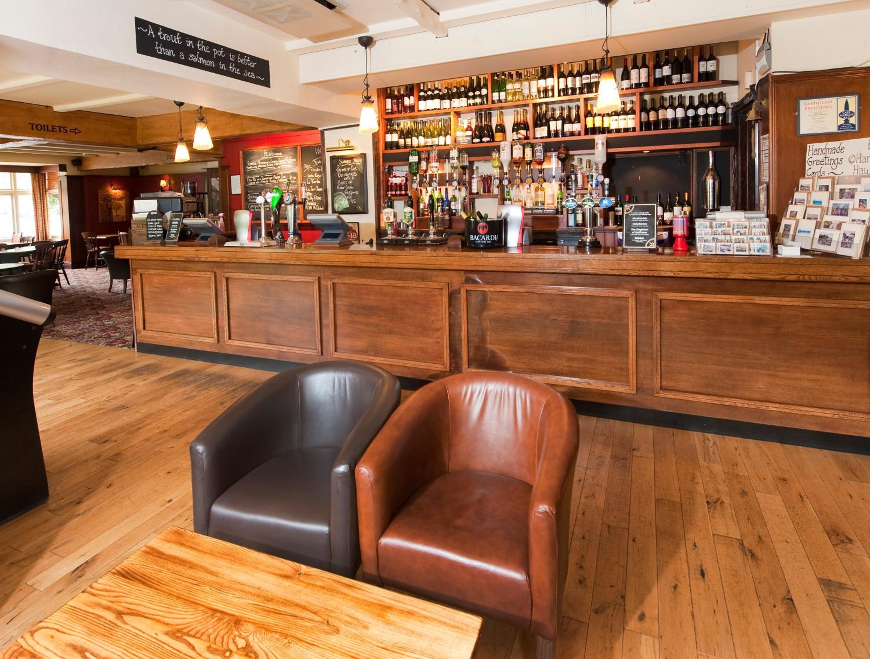 Zona de bar con mobiliario de madera, una vitrina de vinos y licores, y un letrero que indica la ubicación de los baños.