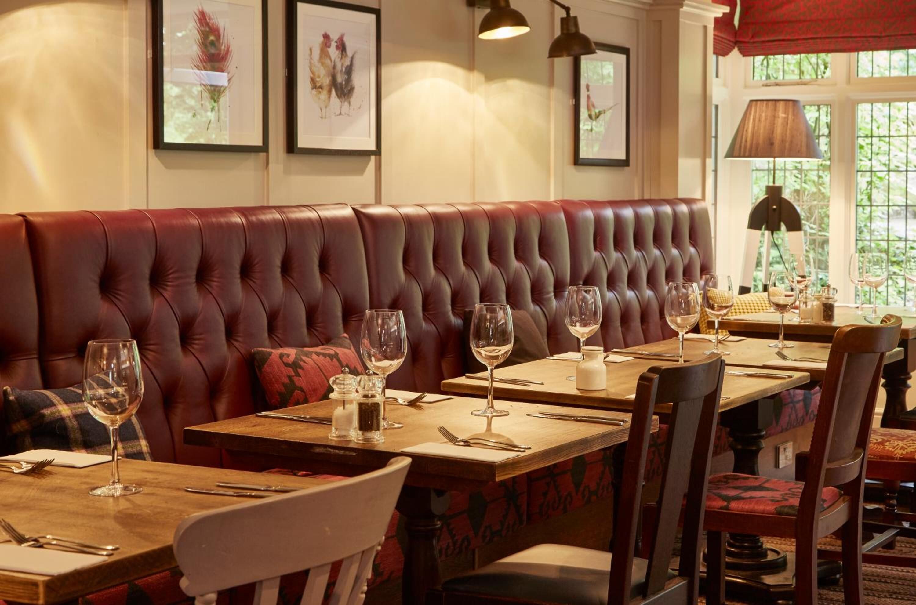A restaurant with a red leather booth, wooden tables, and chairs.