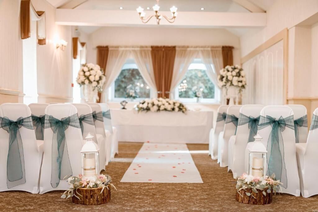 Un pasillo nupcial con sillas blancas, cintas turquesa y decoraciones florales.
