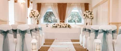 Un pasillo nupcial con sillas blancas, cintas turquesa y decoraciones florales.