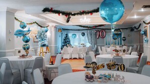 A room with round tables and chairs, a Christmas tree, and balloons. - The Ashburnham Hotel (Burry Port)