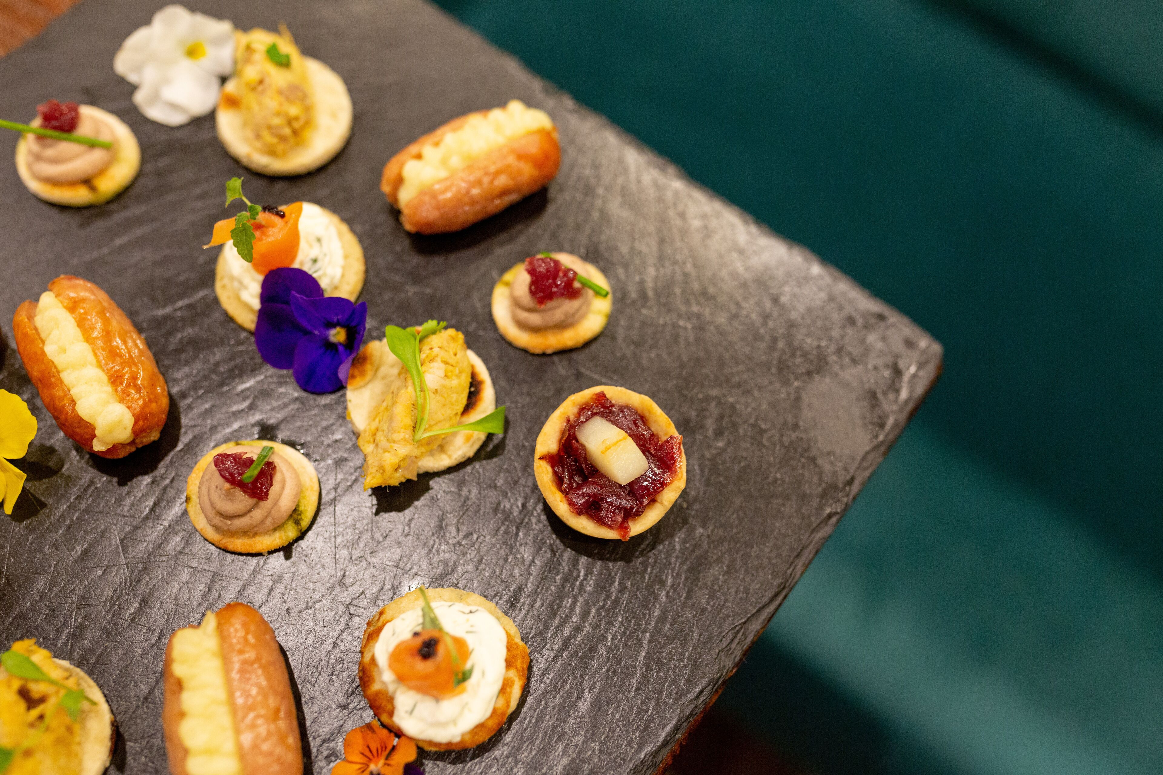 A slate board with various food items, including pastries and desserts, arranged on it.