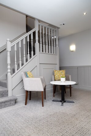 A staircase with white balusters, a round table with a white base, and two chairs with patterned cushions. - Rufford Arms Hotel (Ormskirk)