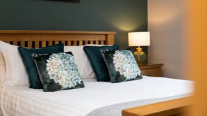 A neatly made bed with floral pillows, a wooden headboard, and a bedside lamp. - Rufford Arms Hotel (Ormskirk)