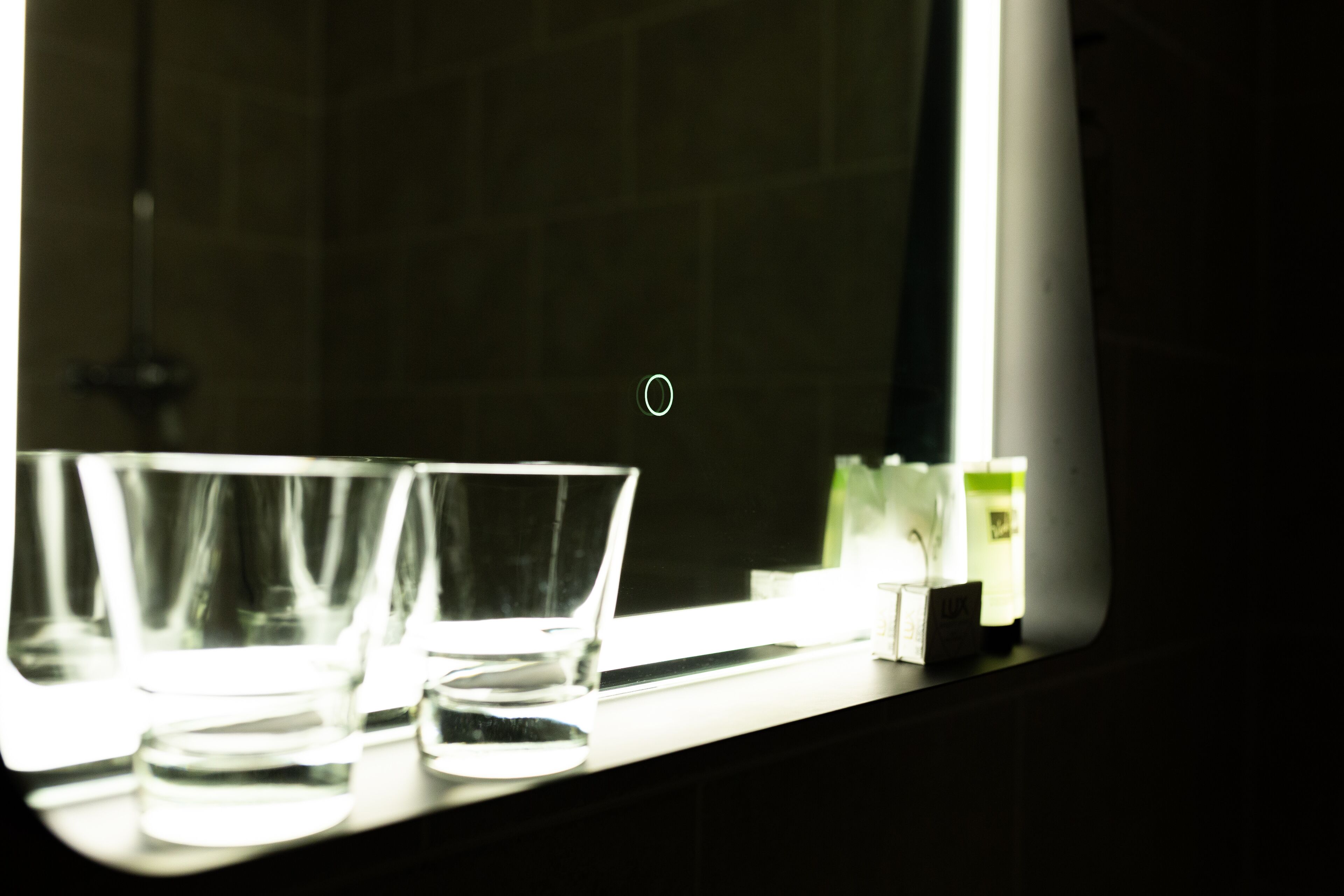 Ett badrum med en spegel som reflekterar tre glas och en liten låda med texten ”LUX” på.